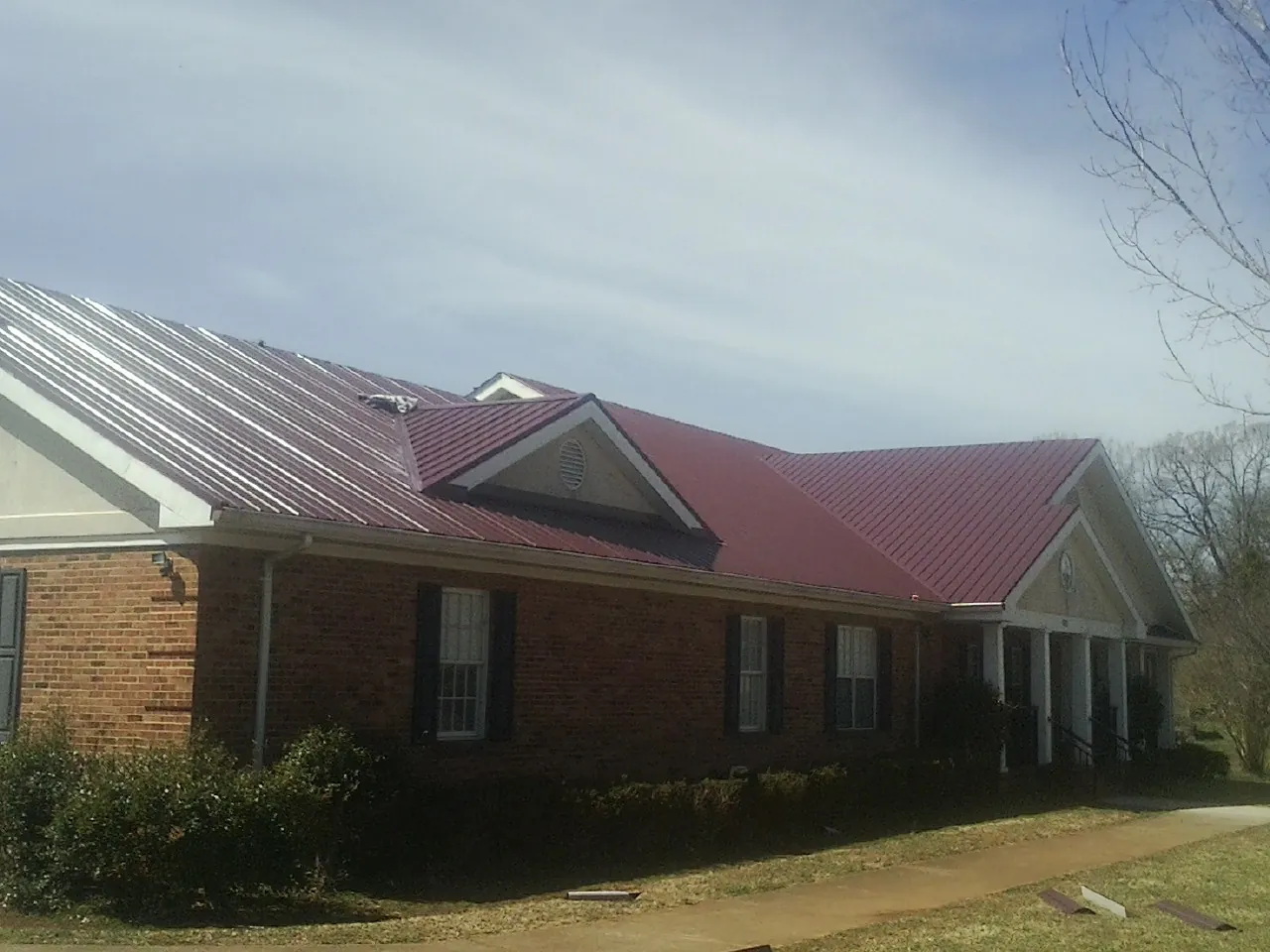 Red metal roof with gabled entries on a long brick building, from a Hail Damage Roof Repair job in Beaver